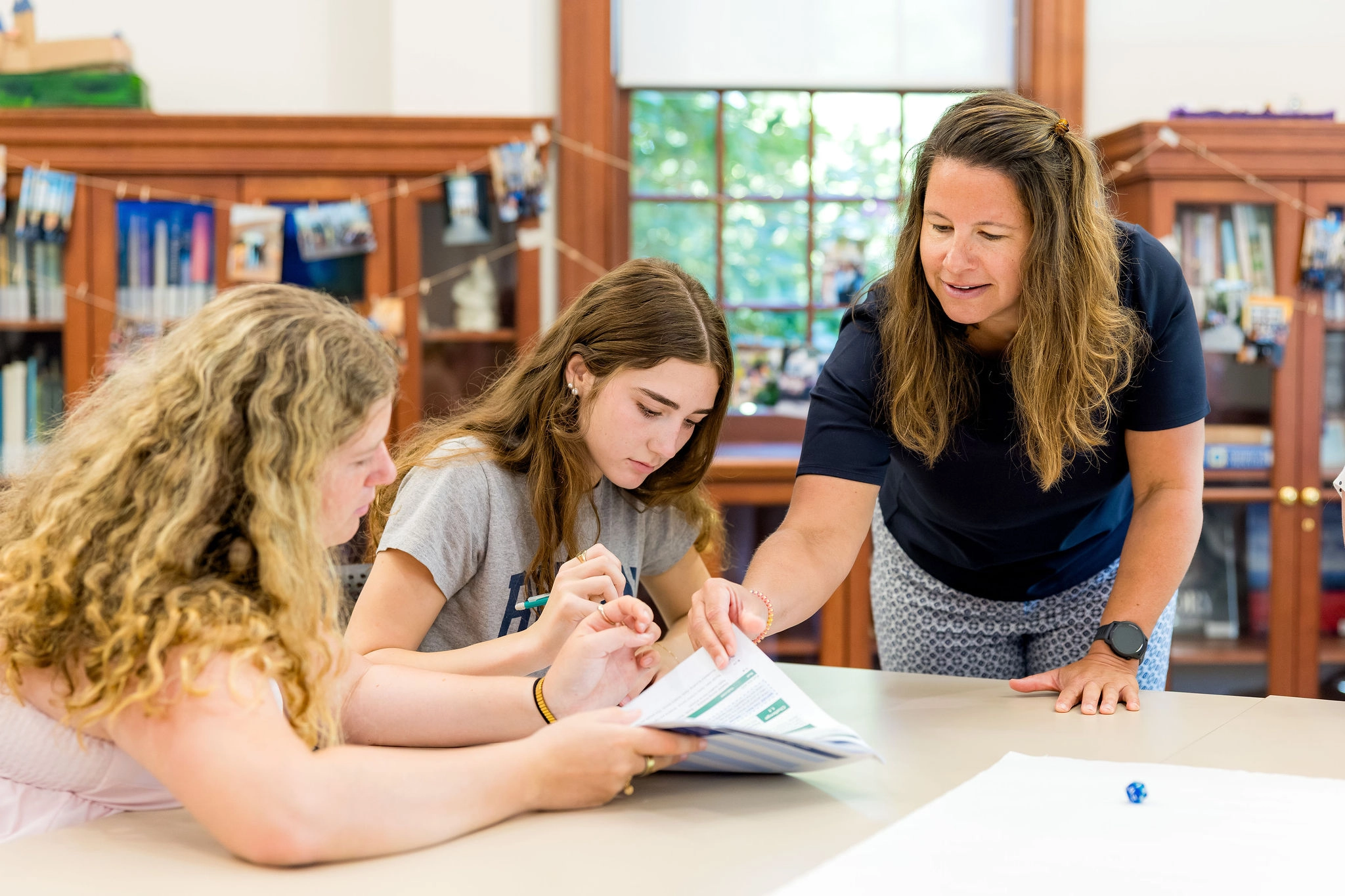 teacher showing two students information on paper at a table desk