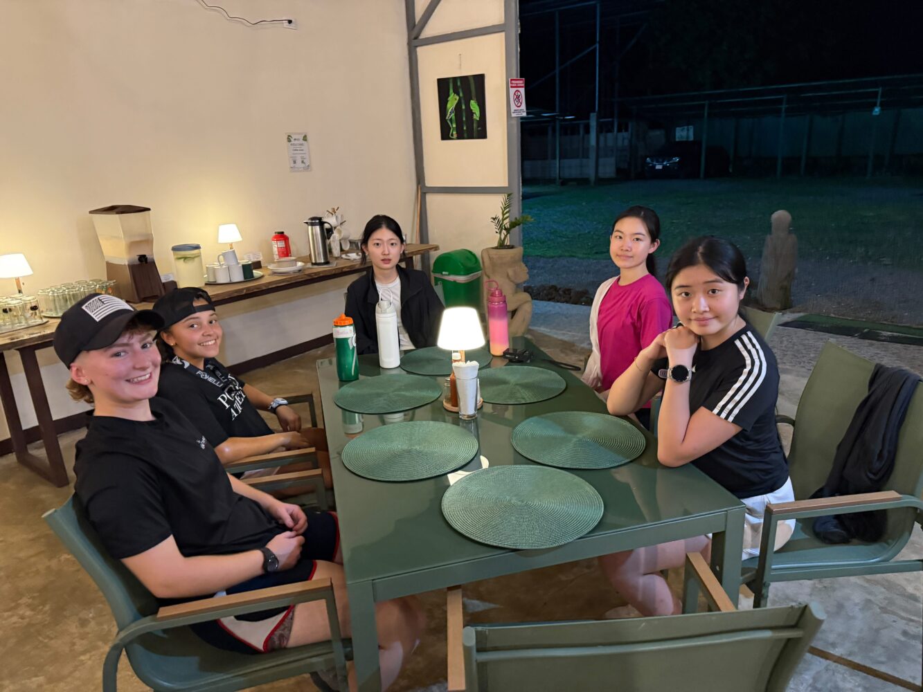 Four young women sit around a green patio table at night.