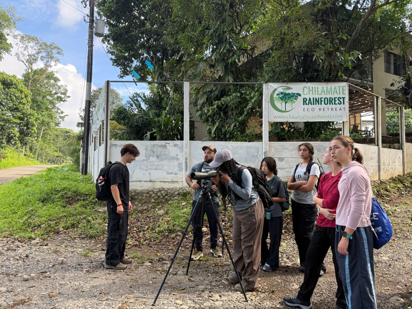 A group of young people at the Chilamate Rainforest Eco Retreat watch through a spotting scope mounted on a tripod.