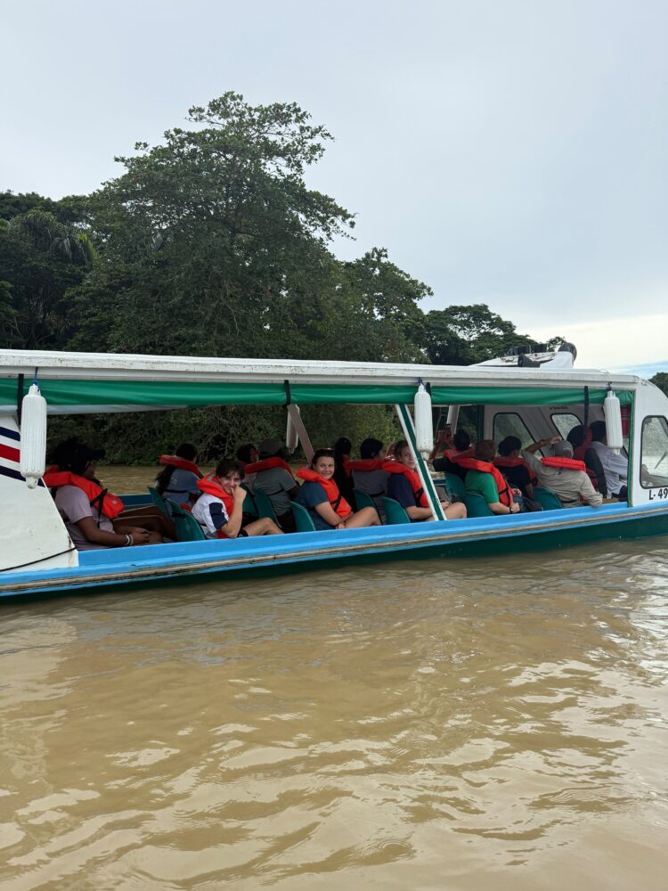 People wearing orange life vests sitting in a boat traveling along a muddy river.