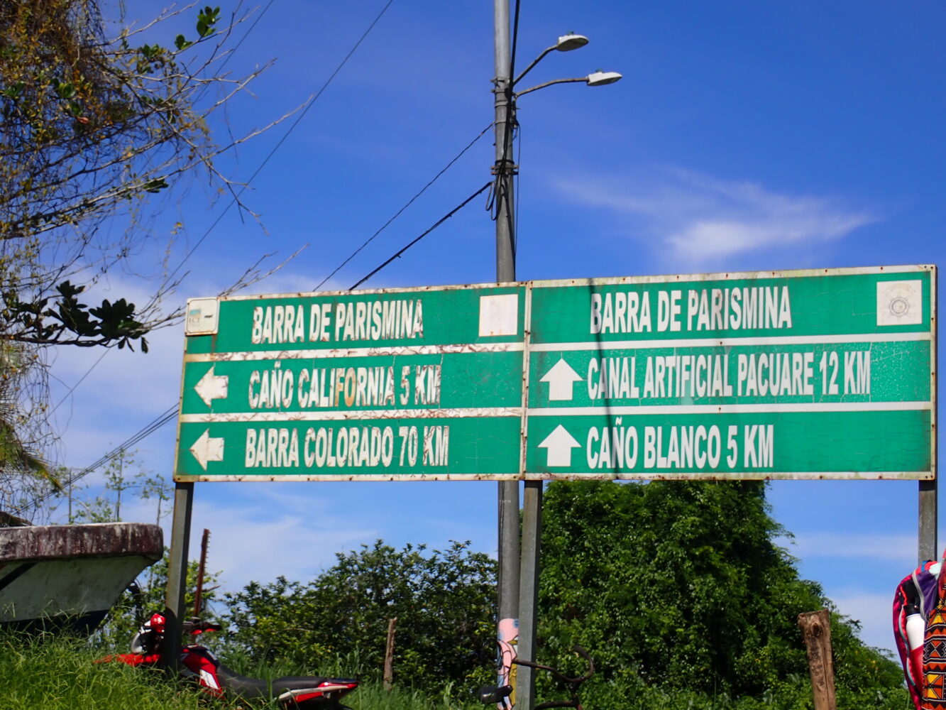 A green road sign lists directions and distances in kilometers to Barra de Parismina, Caño California, Barra Colorado, Canal Artificial Pacuare, and Caño Blanco.