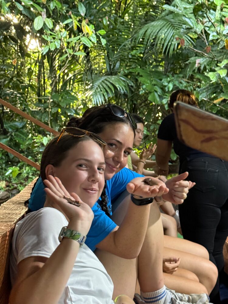 Two young women holding butterflies on their palms in a lush, green forest.