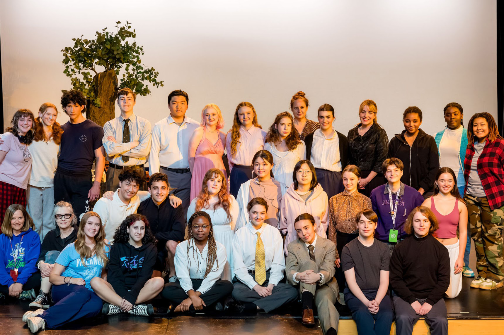 A large group of students and adults posing for a photo on a stage in front of a prop tree.