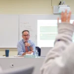 teacher teaching a media literacy course with a student raising their hand