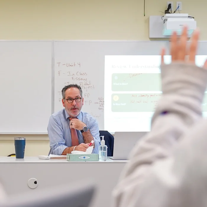 teacher teaching a media literacy course with a student raising their hand