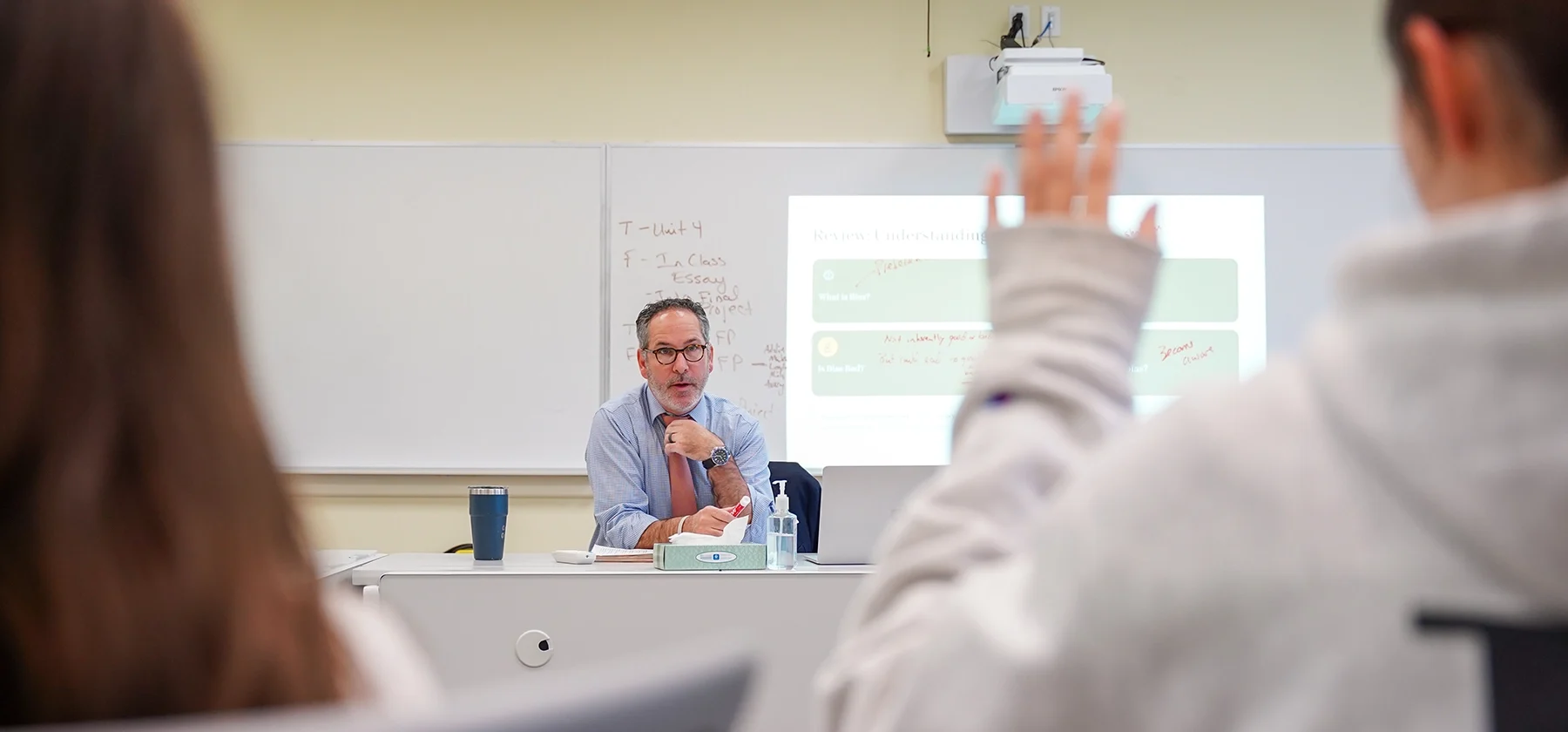 teacher teaching a media literacy course with a student raising their hand